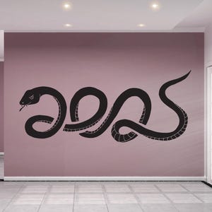 Könnte beinhalten: Ein schwarzer Schlangen-Silhouetten-Wandaufkleber in einer gekrümmten Position. Der Aufkleber befindet sich an einer hellrosa Wand.