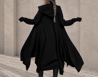 May include: A long, black, hooded cardigan with an asymmetrical hemline and long sleeves featuring thumb holes. The garment is worn over dark leggings and dark brown lace-up boots, creating a layered look with a flowing, draped silhouette.
