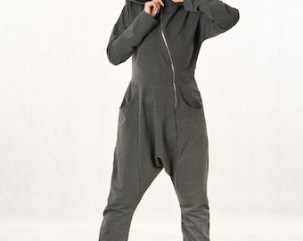 May include: A dark gray jumpsuit featuring a hood, long sleeves, and a diagonal zipper closure that extends from the collar to the waist. The garment includes two side pockets and a drop-crotch design, paired with black lace-up boots.