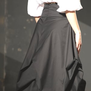 May include: A black skirt with a gathered, voluminous design. The skirt is made of a smooth, lightweight fabric and has a high waist.