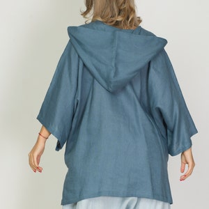 May include: A blue hooded jacket with wide sleeves. The jacket is made of a soft, flowing fabric and is paired with light blue pants. The model is facing away from the camera, showcasing the back of the outfit.