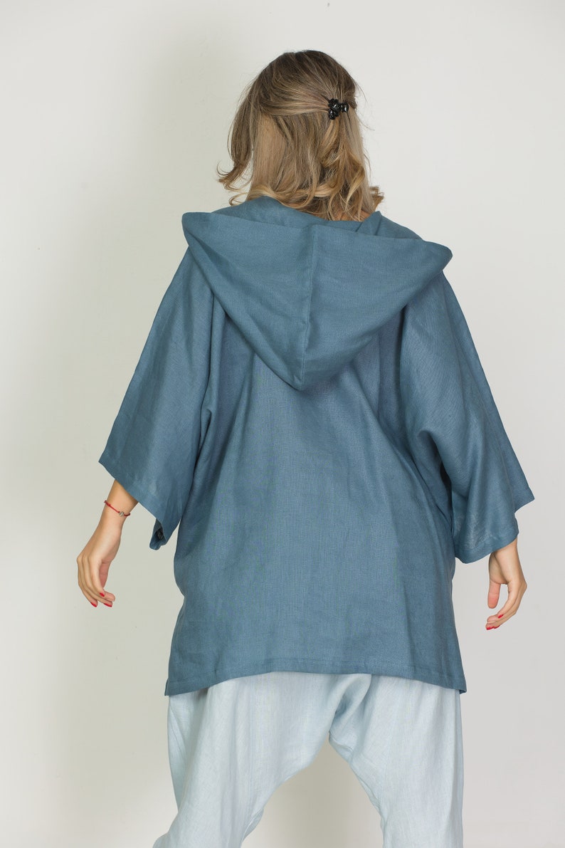 May include: A blue hooded jacket with wide sleeves. The jacket is made of a soft, flowing fabric and is paired with light blue pants. The model is facing away from the camera, showcasing the back of the outfit.