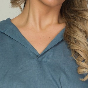 May include: A blue-grey, V-neck top with a relaxed fit. The top features a wide collar and a soft, flowing fabric. The garment is made of a lightweight material, suitable for warmer weather. The design is simple and elegant.
