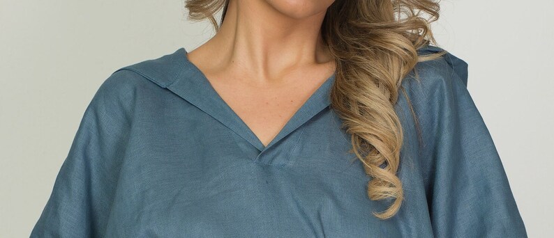 May include: A blue-grey, V-neck top with a relaxed fit. The top features a wide collar and a soft, flowing fabric. The garment is made of a lightweight material, suitable for warmer weather. The design is simple and elegant.