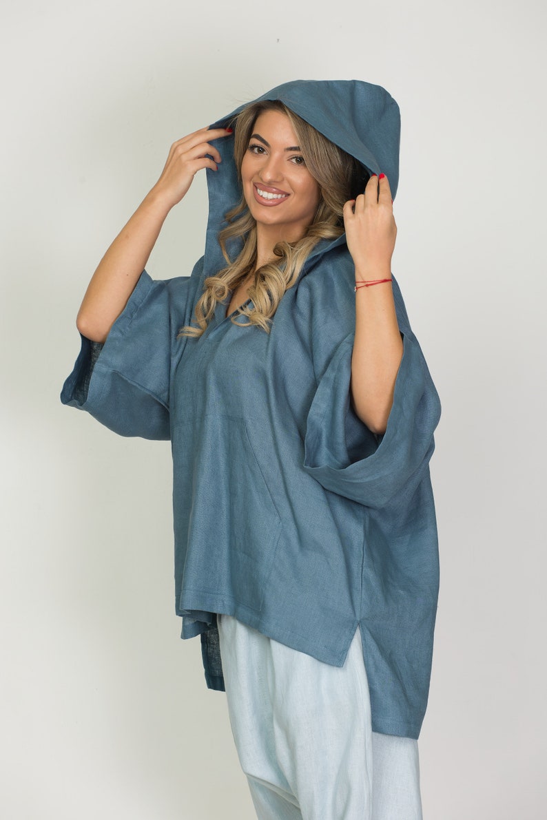 May include: A blue hooded top with wide sleeves. The top has a V-neck and a relaxed fit. The model is wearing the hood up. The top is made of a soft, flowing fabric.