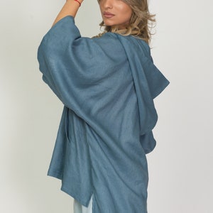 May include: A blue linen kimono-style top with a hood and side slits. The top is a solid color and appears to be made of a lightweight fabric. The model is wearing a light blue outfit.