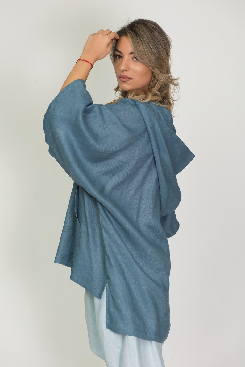 May include: A blue linen kimono-style top with a hood and side slits. The top is a solid color and appears to be made of a lightweight fabric. The model is wearing a light blue outfit.