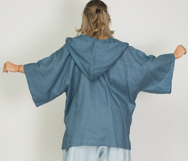 May include: A blue hooded kimono-style top with wide sleeves. The top is made of a lightweight fabric and has a relaxed fit. The hood is attached to the back of the top. The sleeves are wide and extend to the elbows. The top is a solid blue color.
