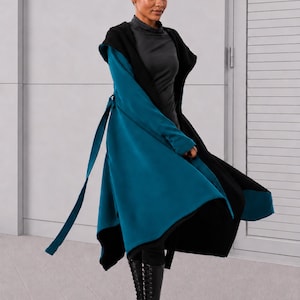 May include: A long-sleeved, hooded coat featuring a vibrant teal exterior and a contrasting black interior lining. The garment includes a matching fabric tie belt at the waist, a flared hemline, and is worn over a dark gray mock neck top and black boots.