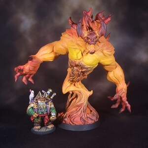 May include: A painted miniature figurine of a large, horned fire elemental with orange and red flames, standing next to a smaller, detailed pirate character figurine wearing a green coat, a hat, and carrying a white bird on its shoulder.