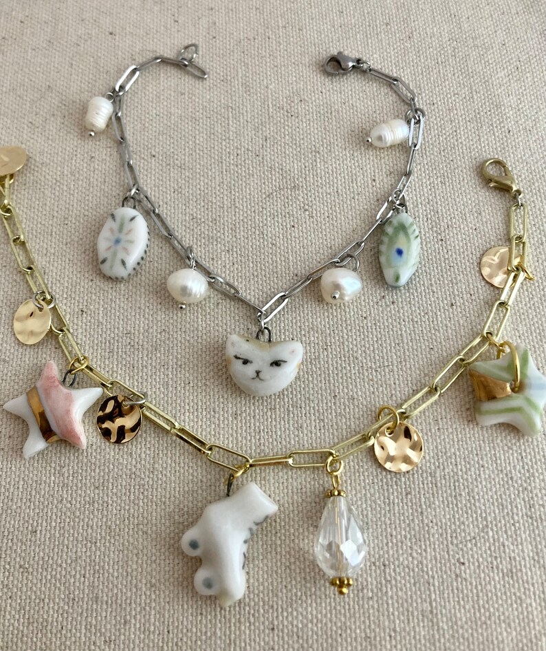 Pu&ograve; includere: Tre braccialetti con ciondoli vari. Un braccialetto &egrave; dorato con ciondoli a forma di stella, disco e orso. Un altro &egrave; argentato con ciondoli a forma di gatto, perla e ovale. Il terzo &egrave; dorato con ciondoli a forma di stella e disco. Lo sfondo &egrave; in tessuto neutro.