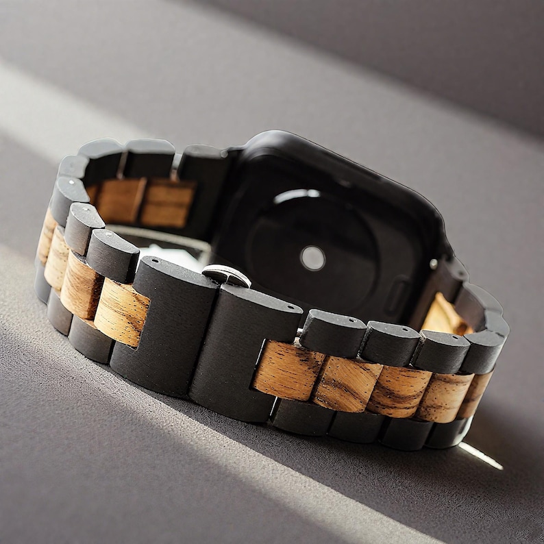 May include: A black smartwatch with a wooden band. The band alternates between dark black and light brown wood segments. The watch is angled, showing the back of the watch and the clasp.