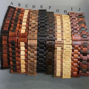 May include: A collection of ten wooden watch bands in various shades of brown, black, and tan. The bands are made of interlocking wooden links, showcasing the natural grain and color variations of the wood. Each band is a different color and wood grain.