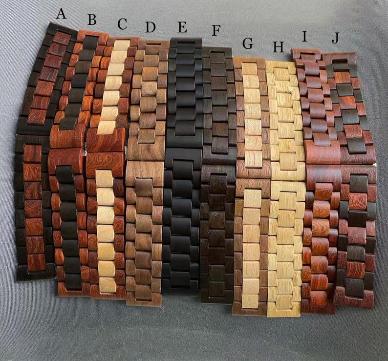 May include: A collection of ten wooden watch bands in various shades of brown, black, and tan. The bands are made of interlocking wooden links, showcasing the natural grain and color variations of the wood. Each band is a different color and wood grain.
