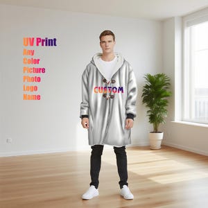 May include: A silver hooded coat with toggle fastenings and the word "CUSTOM" in a gradient font. The coat has a white interior and is worn with black trousers and white trainers. Text on the wall reads "UV Print Any Color Picture Photo Logo Name."