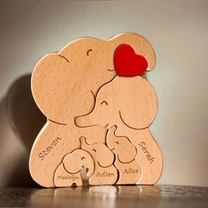 Peut inclure: Puzzle en bois en forme de famille d'&eacute;l&eacute;phants avec un c&oelig;ur rouge sur le dessus. Les &eacute;l&eacute;phants sont &eacute;tiquet&eacute;s avec les noms Steven, Sarah, Alice, Aiden et Madelyn.
