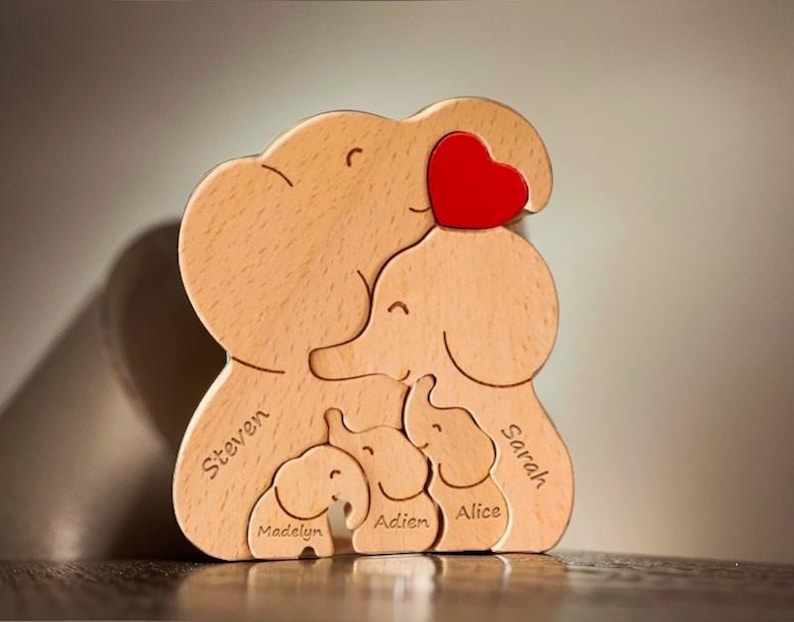 Peut inclure: Puzzle en bois en forme de famille d'&eacute;l&eacute;phants avec un c&oelig;ur rouge sur le dessus. Les &eacute;l&eacute;phants sont &eacute;tiquet&eacute;s avec les noms Steven, Sarah, Alice, Aiden et Madelyn.