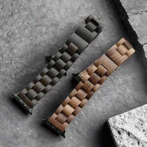 May include: Two watch bands with a wooden design. One band is dark brown, the other is light brown. The bands are made of rectangular wooden blocks. The watch bands are on a gray surface.