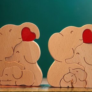Peut inclure: Deux familles d'&eacute;l&eacute;phants en bois, chacune compos&eacute;e de trois &eacute;l&eacute;phants, tiennent des c&oelig;urs rouges. Les &eacute;l&eacute;phants sont empil&eacute;s les uns sur les autres, le plus petit en bas.