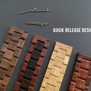 May include: Four wooden watch bands in various shades of brown and tan, with a quick-release design. The bands are made of interlocking wooden blocks. Two silver watch pins are at the top of the image. The text "QUICK RELEASE DESIGN" is in white.