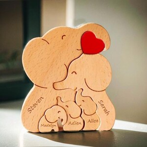 Peut inclure: Puzzle en bois en forme de famille d'&eacute;l&eacute;phants avec les noms Steven, Sarah, Madalyn, Aiden et Alice grav&eacute;s sur chaque &eacute;l&eacute;phant. Les &eacute;l&eacute;phants sont dispos&eacute;s dans une pose d'&eacute;treinte avec un c&oelig;ur rouge sur l'&eacute;l&eacute;phant du haut.