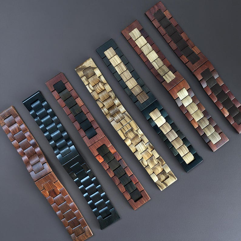 May include: An assortment of wooden watch bands in various colors and wood grains. The bands feature a link design, with colors ranging from light tan to dark brown and black. The bands are arranged diagonally on a gray surface.