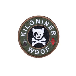 May include: A green and brown circular patch with the text "Kilo Niner Woof" and a white dog with a black spot on its eye and crossed bones.