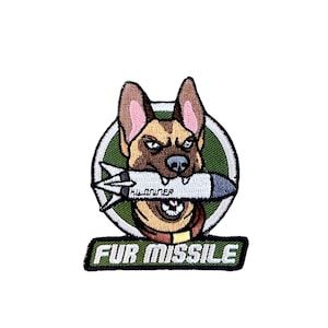 May include: A green and white embroidered patch with a cartoon German Shepherd dog biting a missile. The text "FUR MISSILE" is below the dog.