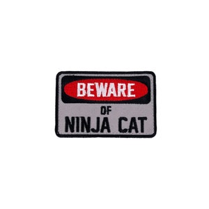 May include: A gray and red warning sign with black text that reads "BEWARE OF NINJA CAT".