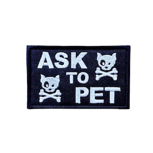 May include: A rectangular black patch with white embroidered text and graphics. The text reads "ASK TO PET" in a bold, sans-serif font. Above and below the word "PET" are skull and crossbones with cat-like features.