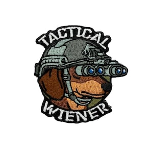 May include: An embroidered patch featuring a brown dachshund wearing a grey tactical helmet with mounted night vision goggles. The text TACTICAL is arched above the helmet and WIENER is arched below, both in white capital letters on black.