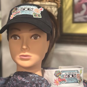 May include: Black visor with a retro "Mix Tape Vol. 1" design featuring a cassette tape, roller skates, and a smiley face. A white visor with the same design is also visible.