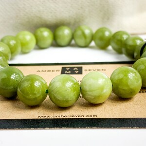 May include: A green jade bracelet with round beads. The bracelet is on a brown card with the text "Amber Seven" and a website address.