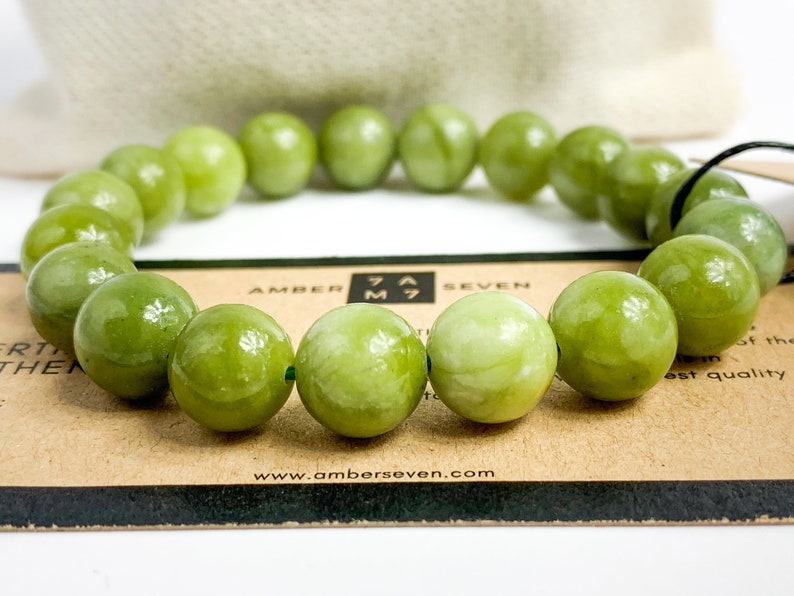 May include: A green jade bracelet with round beads. The bracelet is on a brown card with the text "Amber Seven" and a website address.