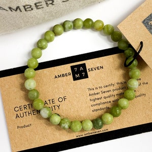 May include: A green jade stone bracelet with a certificate of authenticity card. The card reads "Amber Seven" and "Certificate of Authenticity".
