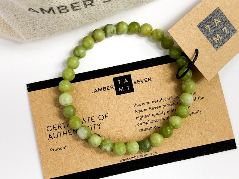 May include: A green jade stone bracelet with a certificate of authenticity card. The card reads "Amber Seven" and "Certificate of Authenticity".
