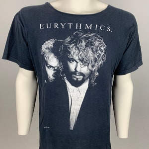 May include: Black t-shirt with a faded image of the band Eurythmics. The band members are pictured in black and white. The text "EURYTHMICS." is printed in white on the shirt.