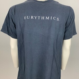 May include: A dark grey t-shirt with the word "EURYTHMICS" printed in white on the back.