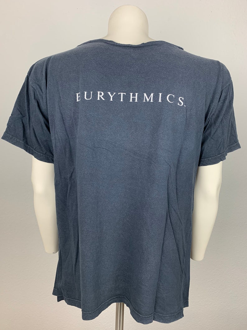 May include: A dark grey t-shirt with the word "EURYTHMICS" printed in white on the back.