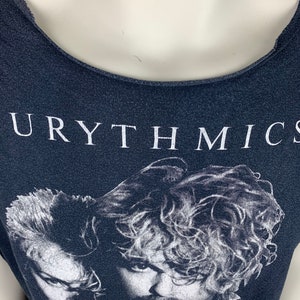 May include: A black t-shirt with a white print of the band Eurythmics. The print features a black and white image of the band members.