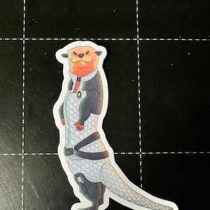 May include: A sticker of a cartoon otter wearing a black and grey spacesuit with a white and grey pattern. The otter has a red nose and a white belly.