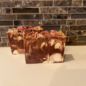 May include: Two bars of handmade soap with a brown and white swirl pattern. The soap has a pink and white swirl on top.