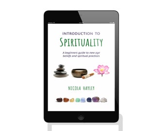 May include: A digital tablet displaying a book cover for "Introduction to Spirituality: A beginners guide to new age beliefs and spiritual practices" by Nicola Hayley. The cover features a stack of stones, a singing bowl, a lotus flower, and a row of colorful gemstones.