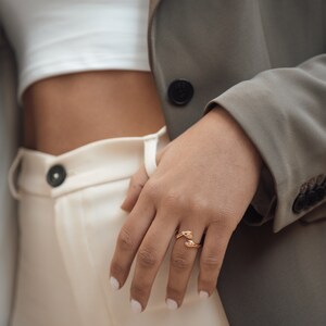 Pu&ograve; includere: Un anello d'oro con un design di due mani intrecciate. L'anello &egrave; indossato sull'anulare di una mano.