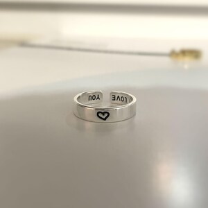 May include: A silver adjustable ring with the words "I LOVE YOU" engraved on the band. A small heart is engraved on the front of the ring.