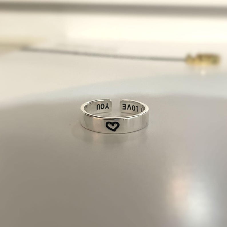 May include: A silver adjustable ring with the words "I LOVE YOU" engraved on the band. A small heart is engraved on the front of the ring.