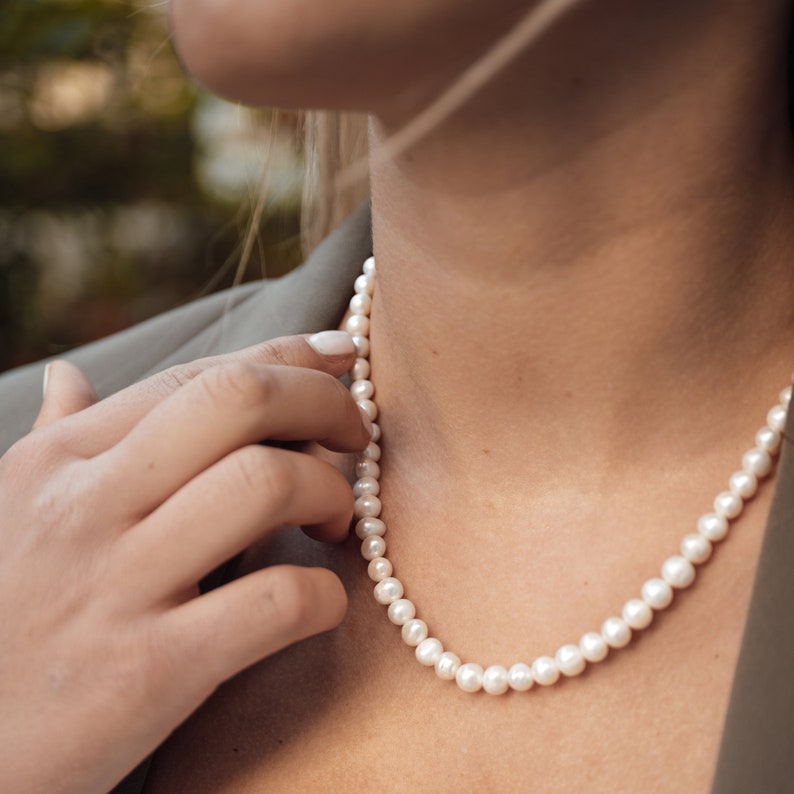 May include: A woman wearing a pearl necklace. The necklace is made of white pearls and is about 18 inches long.