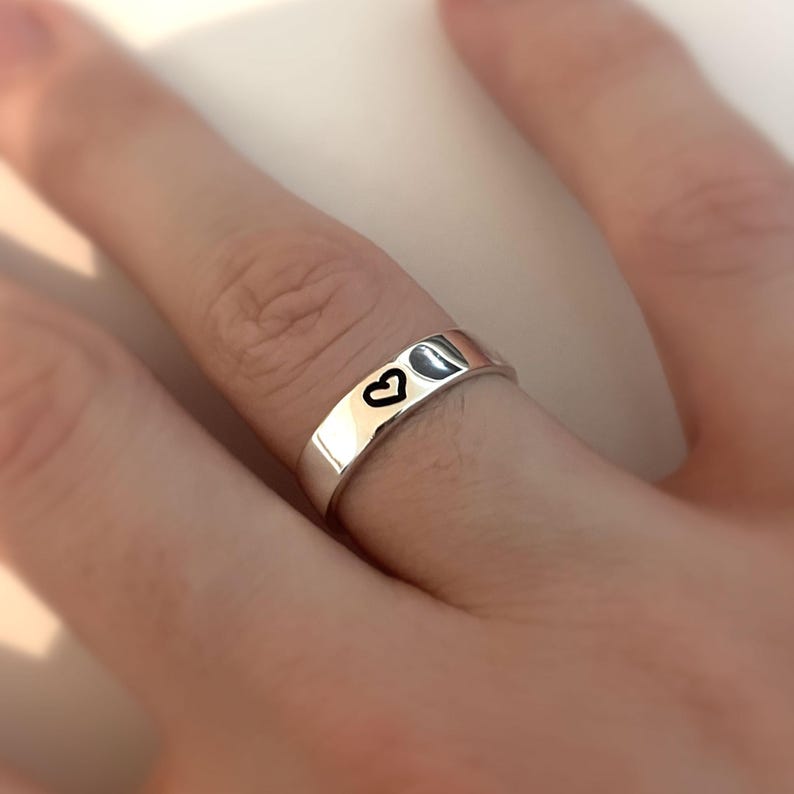 May include: A silver band ring with a small heart design engraved on the side.