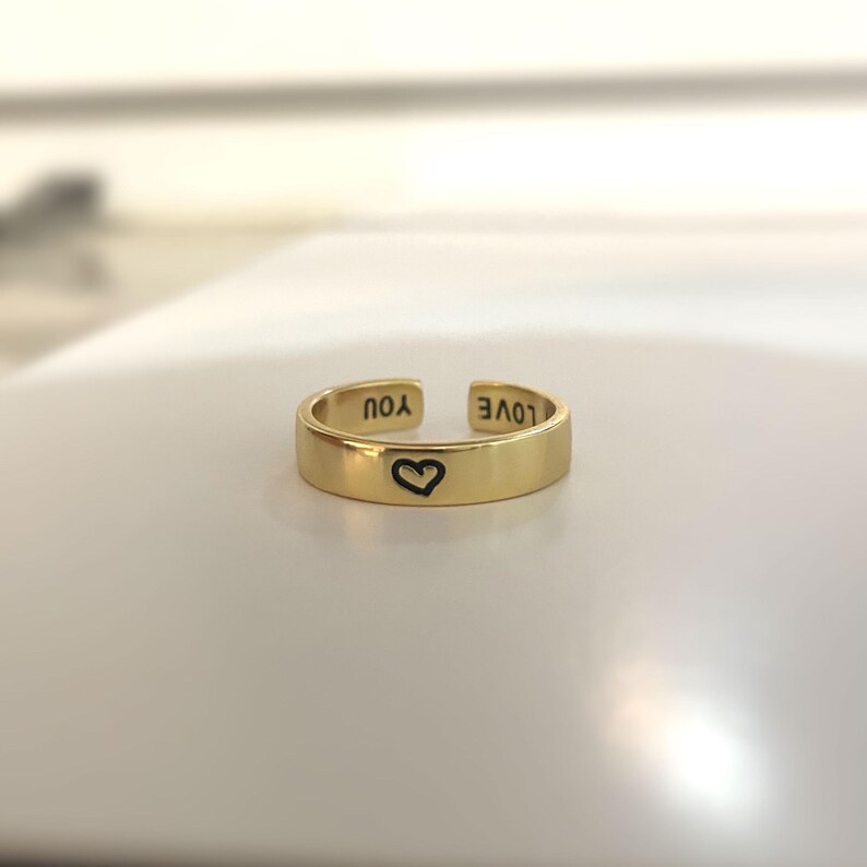 May include: A gold adjustable ring with the words "LOVE" and "YOU" engraved on the outside and a heart symbol engraved on the inside.