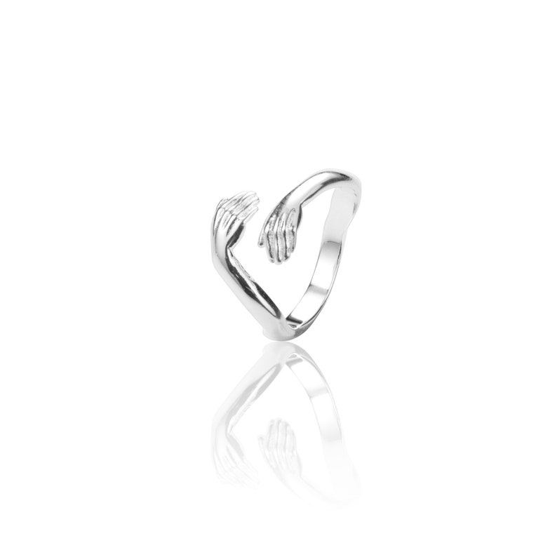 Pu&ograve; includere: Anello d'argento con due mani intrecciate che formano un cuore.